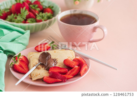 Crepes with chocolate spread and fresh strawberries, served with tea on pink background Crepes with chocolate spread and fresh strawberries, served with tea on pink background 128461753