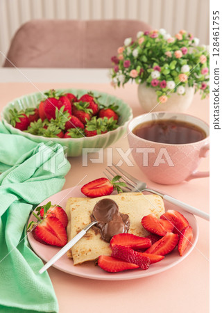 Crepes with chocolate spread and fresh strawberries, served with tea on pink background Crepes with chocolate spread and fresh strawberries, served with tea on pink background 128461755