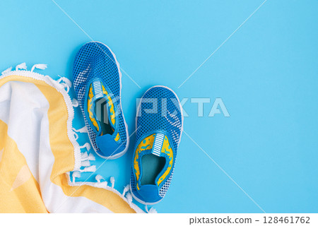Water shoes and a striped towel on a blue background. 128461762