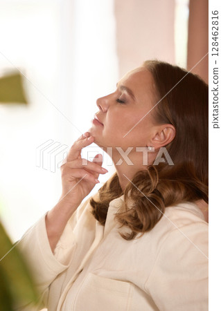 Older woman touching chin with closed eyes in soft natural light expressing peaceful emotion 128462816