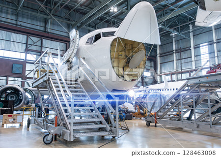 Front view of the white passenger airliner under maintenance in the aircraft hangar. The plane has opened weather radar. Checking mechanical systems for flight operations Front view of the white passenger airliner under maintenance in the aircraft hangar. The plane has opened weather radar. Checking mechanical systems for flight operations 128463008