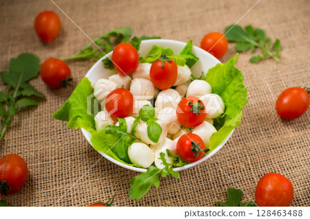mini mozzarella in white bowl with herbs and cherry tomatoes 128463488