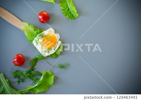 Fried egg with greens on wooden spatula on gray background Fried egg with greens on wooden spatula on gray background 128463491
