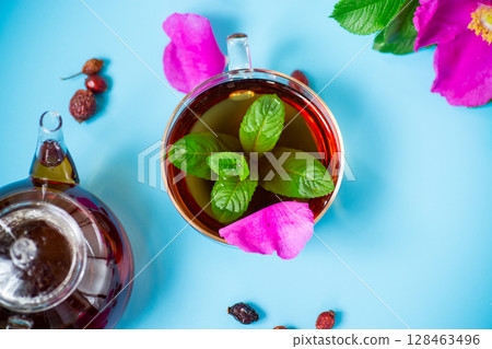 Aesthetic serving of tea with rosehip, petals and mint greens on blue background Aesthetic serving of tea with rosehip, petals and mint greens on blue background 128463496