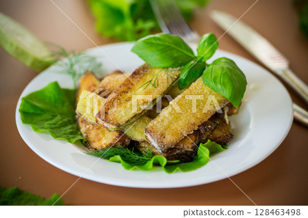 Homemade fried zucchini on a white plate on a brown background Homemade fried zucchini on a white plate on a brown background 128463498