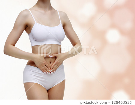 Slim woman in white underwear forming a heart symbol with her hands on her belly against an abstract background with circles and copyspace 128463535