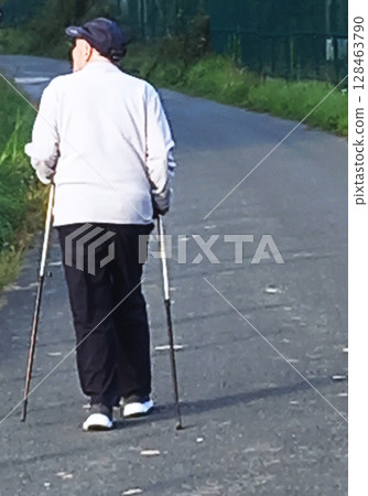 Older man walking through countryside with walking sticks Older man walking through countryside with walking sticks 128463790