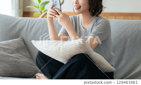 Smiling woman sitting on sofa and using smartphone 128463861