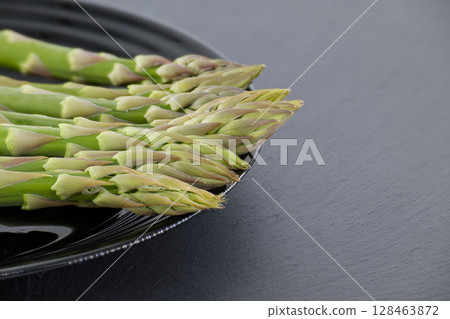 Fresh asparagus spears arranged on a black plate, ready for a healthy meal. Fresh asparagus spears arranged on a black plate, ready for a healthy meal. 128463872