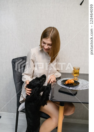 Black cocker spaniel puppy begging for food at breakfast table. 128464099