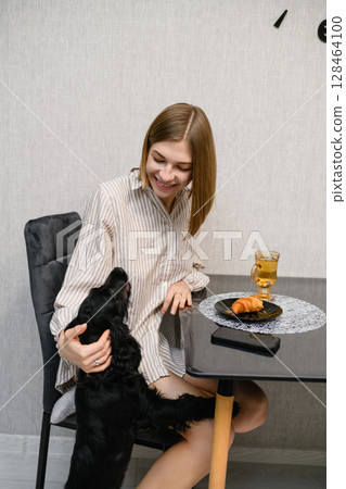 Smiling woman cuddling black cocker spaniel puppy at breakfast table. 128464100