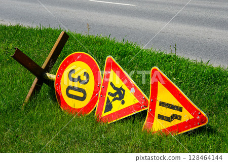 Fallen Road Work Signs on Grass Shoulder Next to Highway Indicating Speed Limit and Road Narrowing 128464144