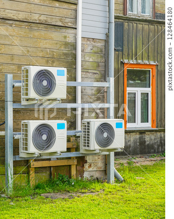 Multiple Air-to-Air Heat Pump Outdoor Units Installed on Wooden Wall of a Residential Building 128464180