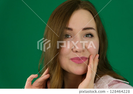 Close-up portrait of a woman with radiant, glowing skin gently touching her face. Her flawless complexion and smooth skin make this image perfect for beauty, makeup, and skincare promotions 128464228
