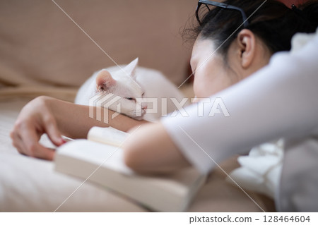 A woman reading and a white cat taking a nap 128464604