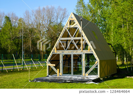 Modern A-Frame Glamping Cabin Under Construction in Scenic Forest Setting on a Sunny Day Modern A-Frame Glamping Cabin Under Construction in Scenic Forest Setting on a Sunny Day 128464664
