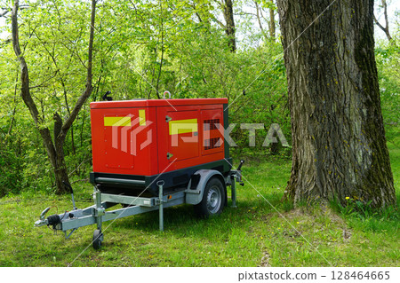 Mobile Red Power Generator Trailer Parked in a Green Forest Clearing Near Large Tree on a Sunny Day Mobile Red Power Generator Trailer Parked in a Green Forest Clearing Near Large Tree on a Sunny Day 128464665