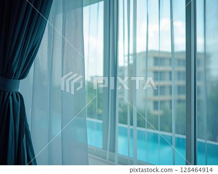 Light filters through sheer curtains revealing a serene view of a poolside apartment complex 128464914