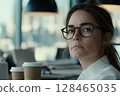 Young woman with glasses contemplating ideas in a modern office setting surrounded by coffee cups 128465035