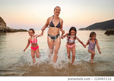 Family enjoys playful moments at the shoreline during sunset 128465118