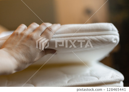 A hand places a plush mattress topper on a bed, enhancing the sleeping surface for better comfort. The soft bedding adds style and warmth to the space, perfect for restful nights A hand places a plush mattress topper on a bed, enhancing the sleeping surface for better comfort. The soft bedding adds style and warmth to the space, perfect for restful nights 128465441