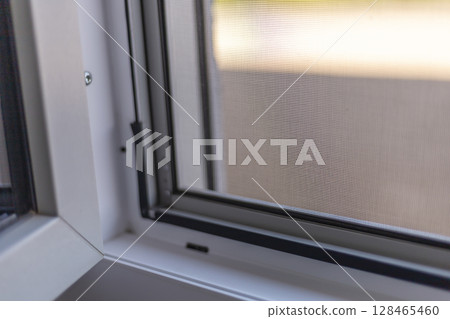 Detailed view of a window frame featuring a mesh screen that offers fly protection. Sunlight filters through, creating a warm and inviting atmosphere as installation is in progress Detailed view of a window frame featuring a mesh screen that offers fly protection. Sunlight filters through, creating a warm and inviting atmosphere as installation is in progress 128465460