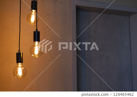 Three stylish pendant lights emit a warm glow in a contemporary setting. The soft illumination highlights the minimalist design of the space, creating a cozy atmosphere Three stylish pendant lights emit a warm glow in a contemporary setting. The soft illumination highlights the minimalist design of the space, creating a cozy atmosphere 128465462