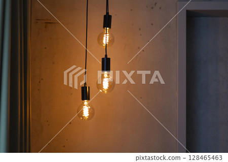 Three warm light bulbs hang from black cables, illuminating a textured wall in a contemporary room. The glow creates a cozy atmosphere, enhancing the space's design 128465463