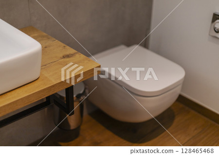 A clean and modern bathroom showcases a contemporary toilet beside a wooden countertop with a white sink. The space is bright and uncluttered, emphasizing simplicity and style A clean and modern bathroom showcases a contemporary toilet beside a wooden countertop with a white sink. The space is bright and uncluttered, emphasizing simplicity and style 128465468