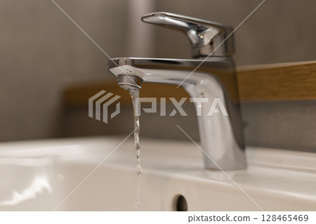 Modern faucet releases a steady stream of water into a clean white sink, showcasing elegant design in a stylish bathroom environment, with a soothing aesthetic 128465469