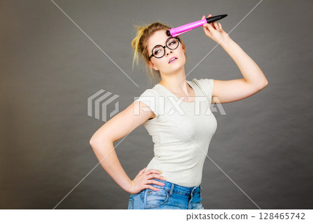 Woman holding big oversized pencil thinking about something Woman holding big oversized pencil thinking about something 128465742