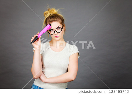 Woman holding big oversized pencil thinking about something Woman holding big oversized pencil thinking about something 128465743