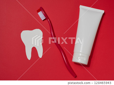 Red toothbrush, white tube of toothpaste and white paper tooth cut out on red background. Red toothbrush, white tube of toothpaste and white paper tooth cut out on red background. 128465943
