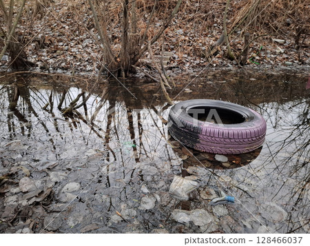 Old rubber tyre lies on river bank, abuse of environment 128466037