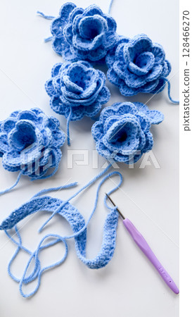 Handmade blue crochet flowers with yarn and hook on white surface 128466270