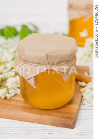 Sweet honey jar surrounded spring acacia blossoms. Honey flows from a spoon in a jar. jars of clear fresh acacia honey on wooden background Sweet honey jar surrounded spring acacia blossoms. Honey flows from a spoon in a jar. jars of clear fresh acacia honey on wooden background 128466359