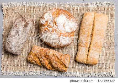 Assortment of freshly baked bread with napkin on rustic table top view. Healthy unleavened bread. French bread Assortment of freshly baked bread with napkin on rustic table top view. Healthy unleavened bread. French bread 128466382