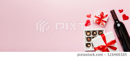Bottle of red wine on colored background for Valentine Day with gift and chocolate. Heart shaped with gift box of chocolates top view with copy space 128466385