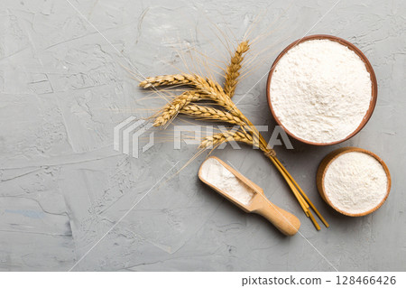 Flat lay of Wheat flour in wooden bowl with wheat spikelets on colored background. world wheat crisis Flat lay of Wheat flour in wooden bowl with wheat spikelets on colored background. world wheat crisis 128466426