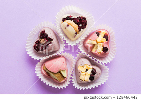 chocolate sweets in the form of a heart with fruits and nuts on a colored background. top view with space for text, holiday concept chocolate sweets in the form of a heart with fruits and nuts on a colored background. top view with space for text, holiday concept 128466442