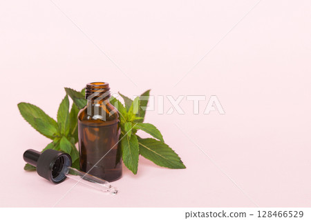Natural Mint Essential Oil in a Glass Bottle. organic cosmetics with herbal extracts of mint on colored background 128466529
