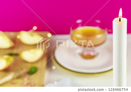 Burning white candle on a blurry kitchen background with apples, honey and lights. Rosh hashanah, Jewish New Year holiday. Selective focus. Jewish holiday background 128466754