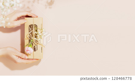 Female hands holding craft gift box with tender flowers on pink background. Romantic holiday background for website. Packaging and delivery concept. Pastel gamma. Flat lay, copy space 128466778