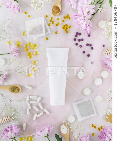 Self care composition with white cosmetic tube with natural cream, herbal tea bags, organic vitamins and supplements with flowers. Organic beauty products and beauty care and treatment concept. Mockup 128466787