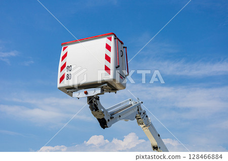 Construction workers utilize a raised platform for maintenance tasks in an open area under clear skies and bright sunlight 128466884