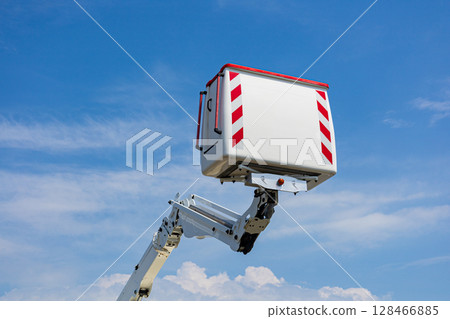 Work platform raised high against a blue sky with clouds, ready for maintenance tasks in an outdoor environment during daylight 128466885