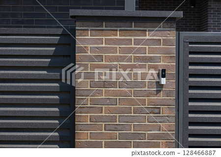 A brick wall with a modern design features a sleek gate and an intercom, showcasing contemporary architectural style during the day 128466887