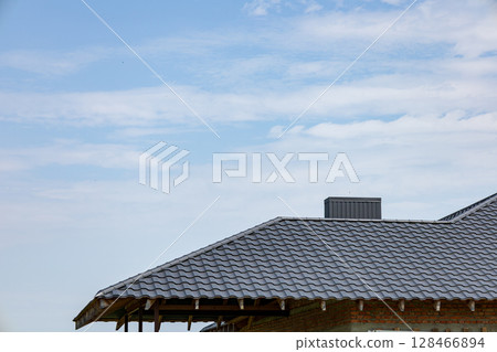 Construction workers are installing new metallic tiles on the rooftops of a building while the sky features soft, scattered clouds 128466894