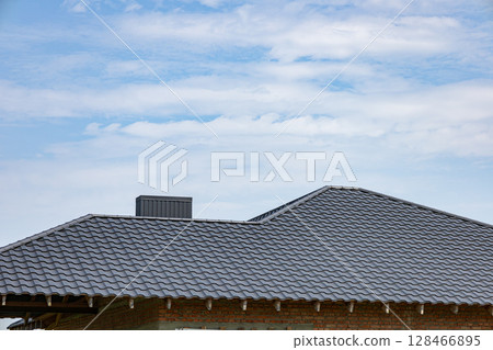 Metallic tiled rooftop showcases durable roofing materials under a clear blue sky, highlighting craftsmanship in construction Metallic tiled rooftop showcases durable roofing materials under a clear blue sky, highlighting craftsmanship in construction 128466895