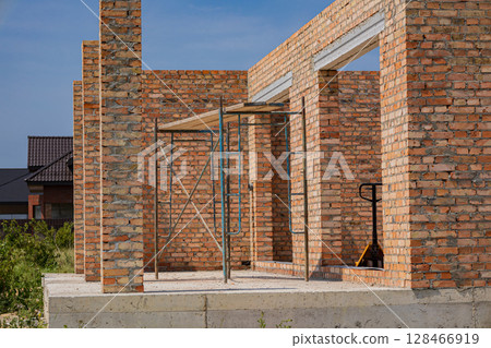 Workers are constructing a brick building in a residential neighborhood under a clear blue sky. Scaffolding is set up for support Workers are constructing a brick building in a residential neighborhood under a clear blue sky. Scaffolding is set up for support 128466919